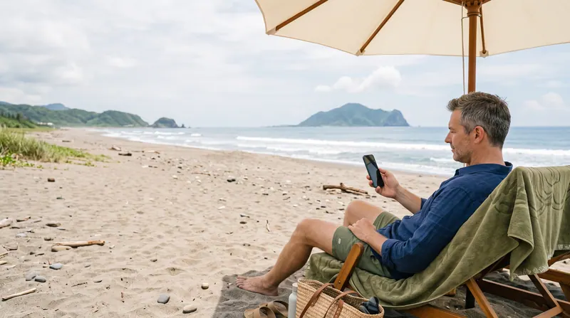 A man in a beach chair under an umbrella, glancing at his phone
