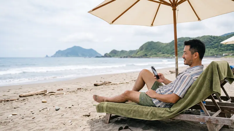 Một người nằm trên ghế dưới ô che nắng ở bãi biển, liếc nhìn điện thoại